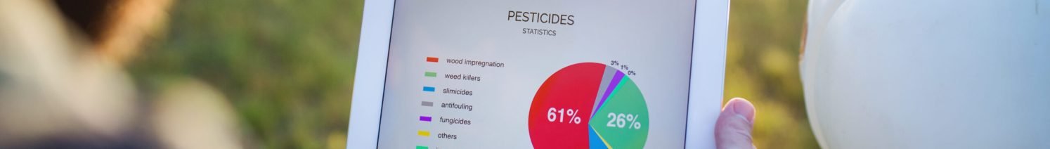 A midsection of mature farmer with tablet standing by mini tractor outdoors in orchard, checking pesticides statistics.